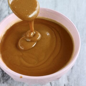 Vegan caramel sauce in a bowl with a spoon lifting up a spoonful of it