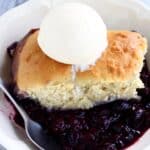 A portion of Vegan Blueberry Cobbler in a bowl with a scoop of vanilla ice cream