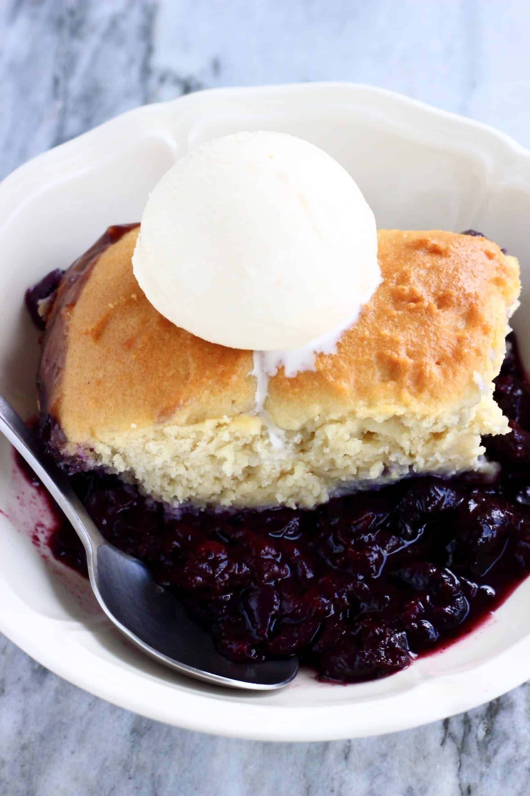 A portion of Vegan Blueberry Cobbler in a bowl with a scoop of vanilla ice cream